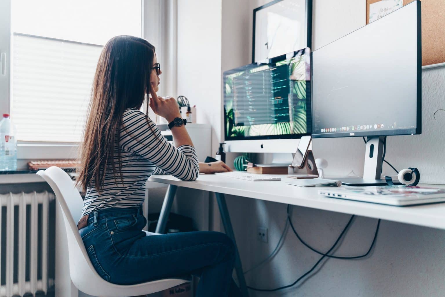 A woman sits at a desk with two monitors, a laptop and a smartphone