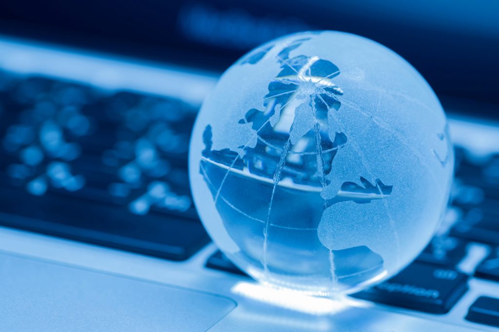 A glass world globe on the keyboard of a laptop representing a concept of digital twins