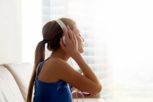 Young woman in headphones is relaxing while listening to music, audio podcast or a mediation session at home