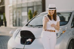 Charging electro car at the electric gas station. Woman standing by the car.