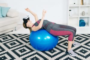 A young woman wearing VR glasses is stretching pilates ball